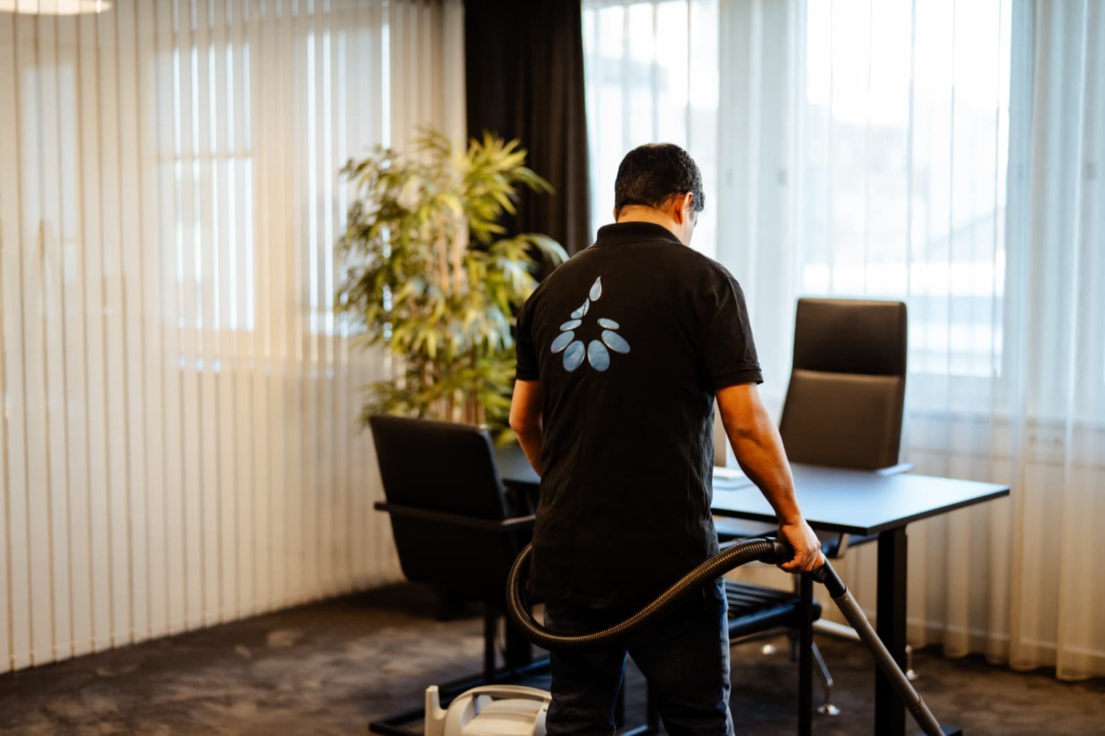 Living Clean renholder utfører støvsuging av kontorgulv ved arbeidsstasjoner